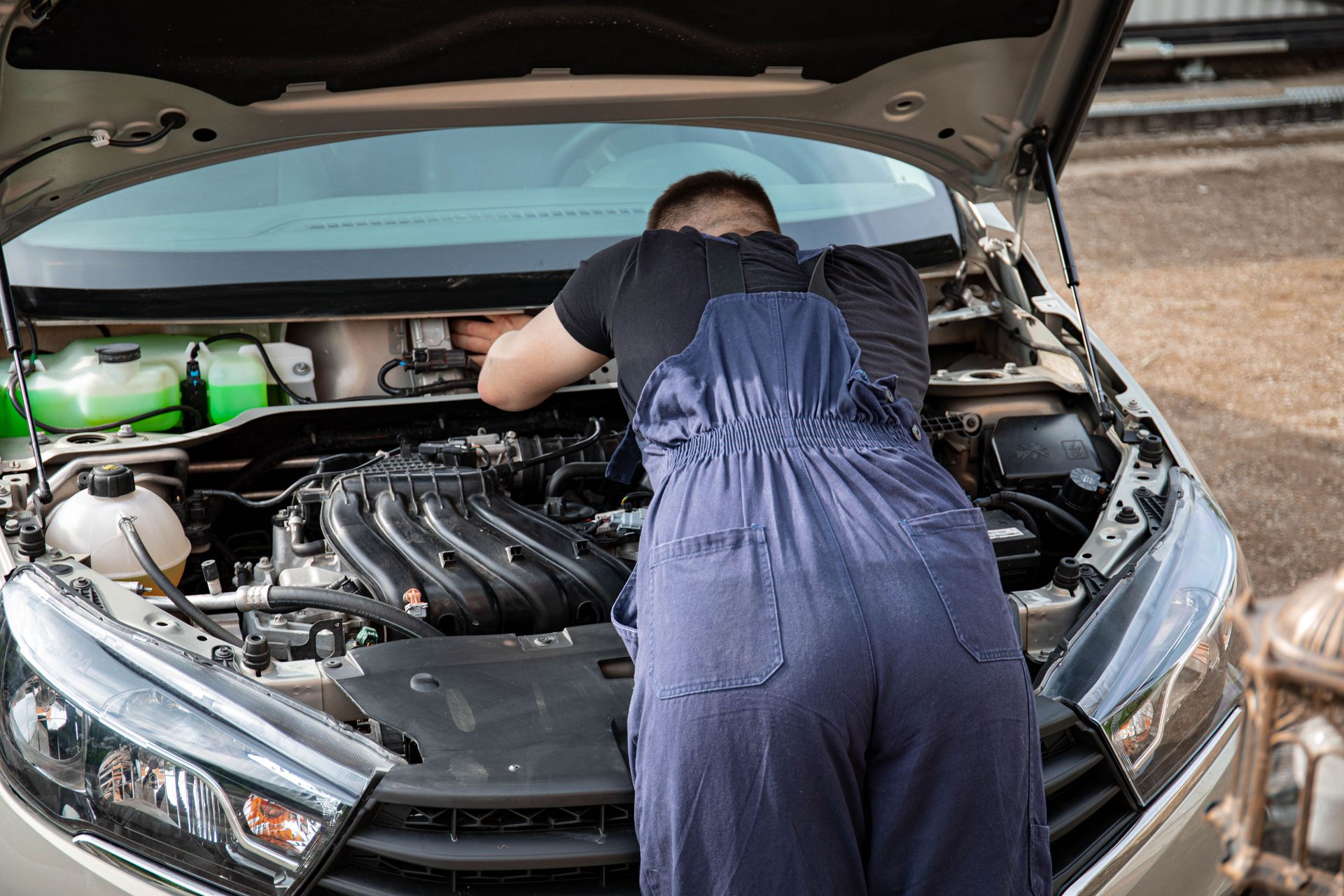 An automotive mechanic performing engine maintenance on a car outdoors, showcasing mechanical skills.