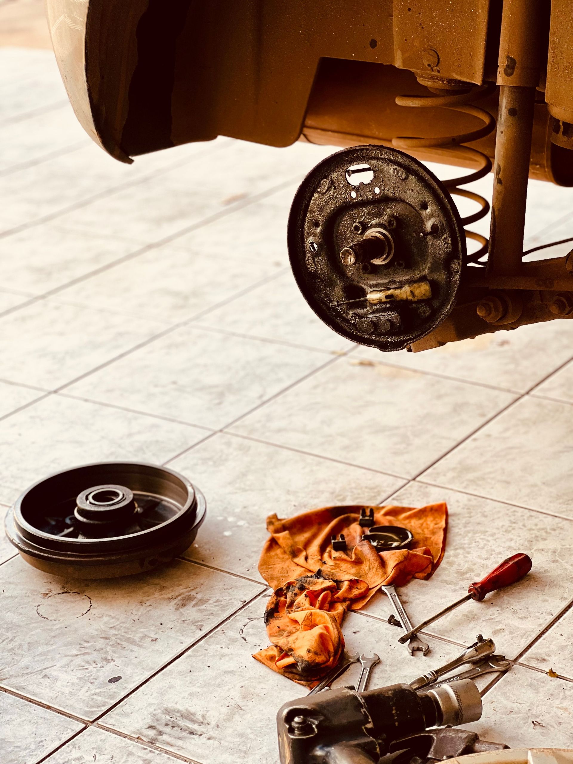 Close-up of a dismantled car brake rotor and tools on a garage floor, illustrating auto repair.